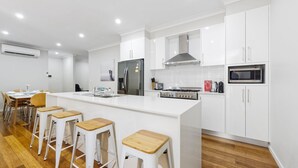 Eine moderne Küche mit weißen Schränken, einer zentralen Kochinsel mit Barhocker, einem Edelstahl-Kühlschrank, einer Mikrowelle und einem Gasherd.