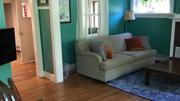 Ein Wohnzimmer mit türkisfarbenen Wänden, einem beigen Sofa, Holzboden und einem Fenster mit Vorhängen.