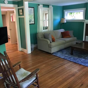 Ein Wohnzimmer mit türkisfarbenen Wänden, einem beigen Sofa, Holzboden und einem Fenster mit Vorhängen.