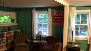 Ein Wohnzimmer mit Holzboden, einem gestreiften Sessel, einem braunen Sessel, einem Couchtisch, einem Bücherregal und einem Fenster mit Vorhängen.
