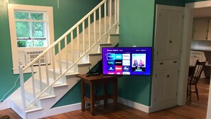 Ein Wohnzimmer mit türkisfarbenen Wänden, einer Holztreppe, einem Flachbildfernseher auf einem Holzboden und einem blau gemusterten Teppich.