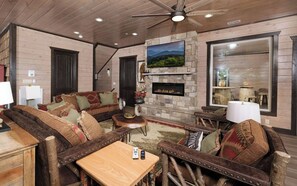 Un salon chaleureux avec une cheminée en pierre, des meubles en bois et un grand téléviseur fixé au mur.