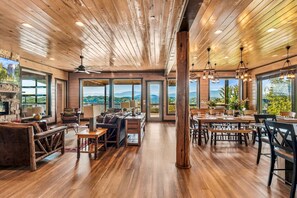 A spacious interior with a wooden ceiling, large windows offering mountain views, a dining area with tables and chairs, and a seating area with sofas and a fireplace. - Paradise Mountain Retreat - Theater Room, Indoor Pool, Wi-Fi & Pool Table (Sevierville)