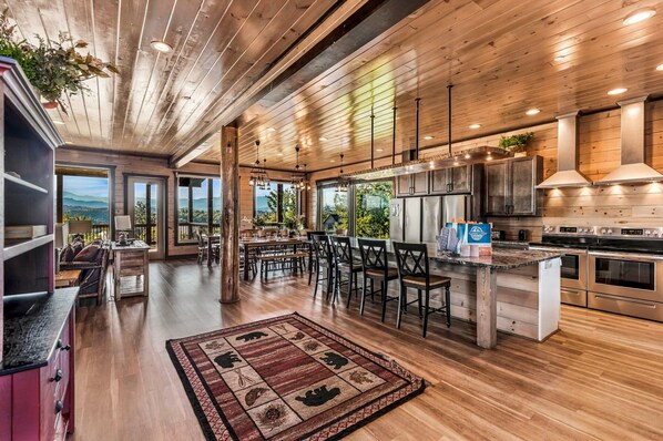 A spacious kitchen with wooden flooring, a central island, and a large window overlooking a scenic landscape.