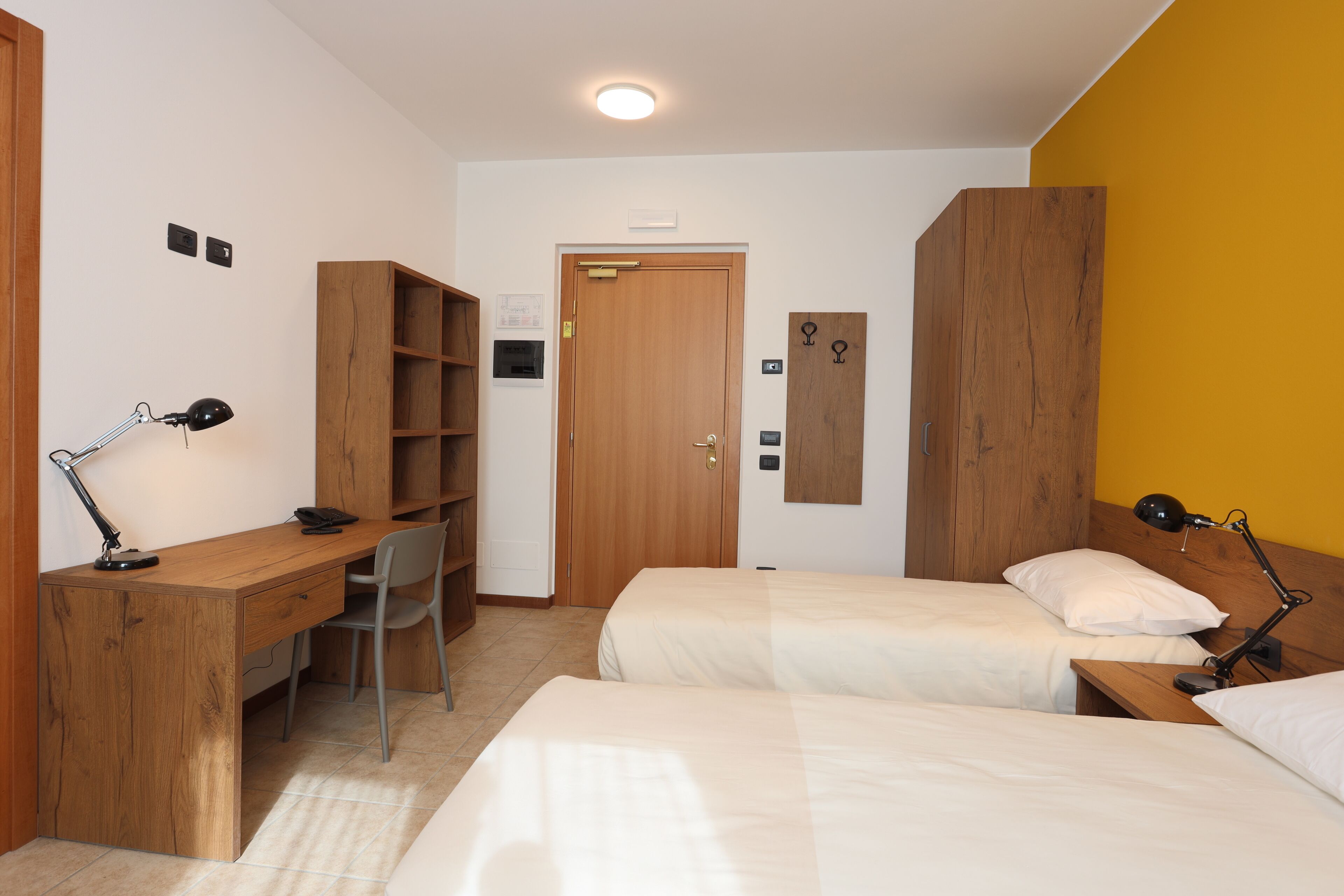 Ein Zimmer mit einem Holztisch, zwei Betten, einem Sessel und einem Kleiderschrank.