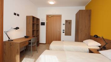 Ein Zimmer mit einem Holztisch, zwei Betten, einem Sessel und einem Kleiderschrank.