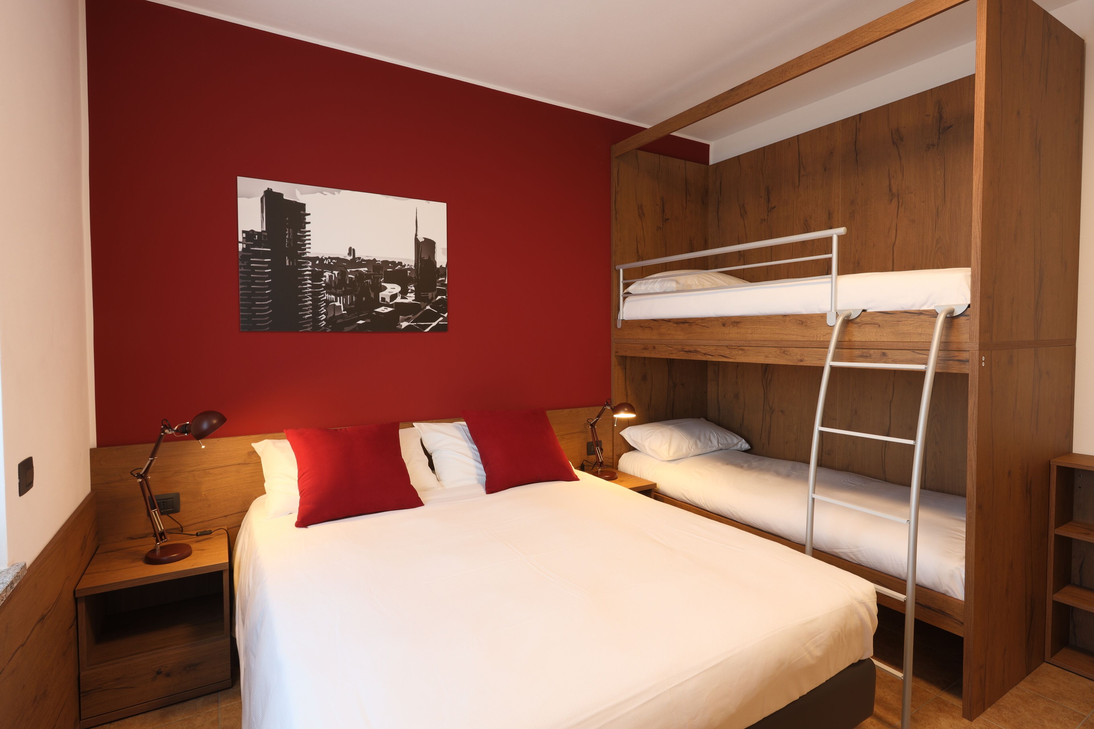 Una habitación con una cama individual, una cama litera, una mesita de noche con una lámpara y una fotografía de la ciudad en la pared.