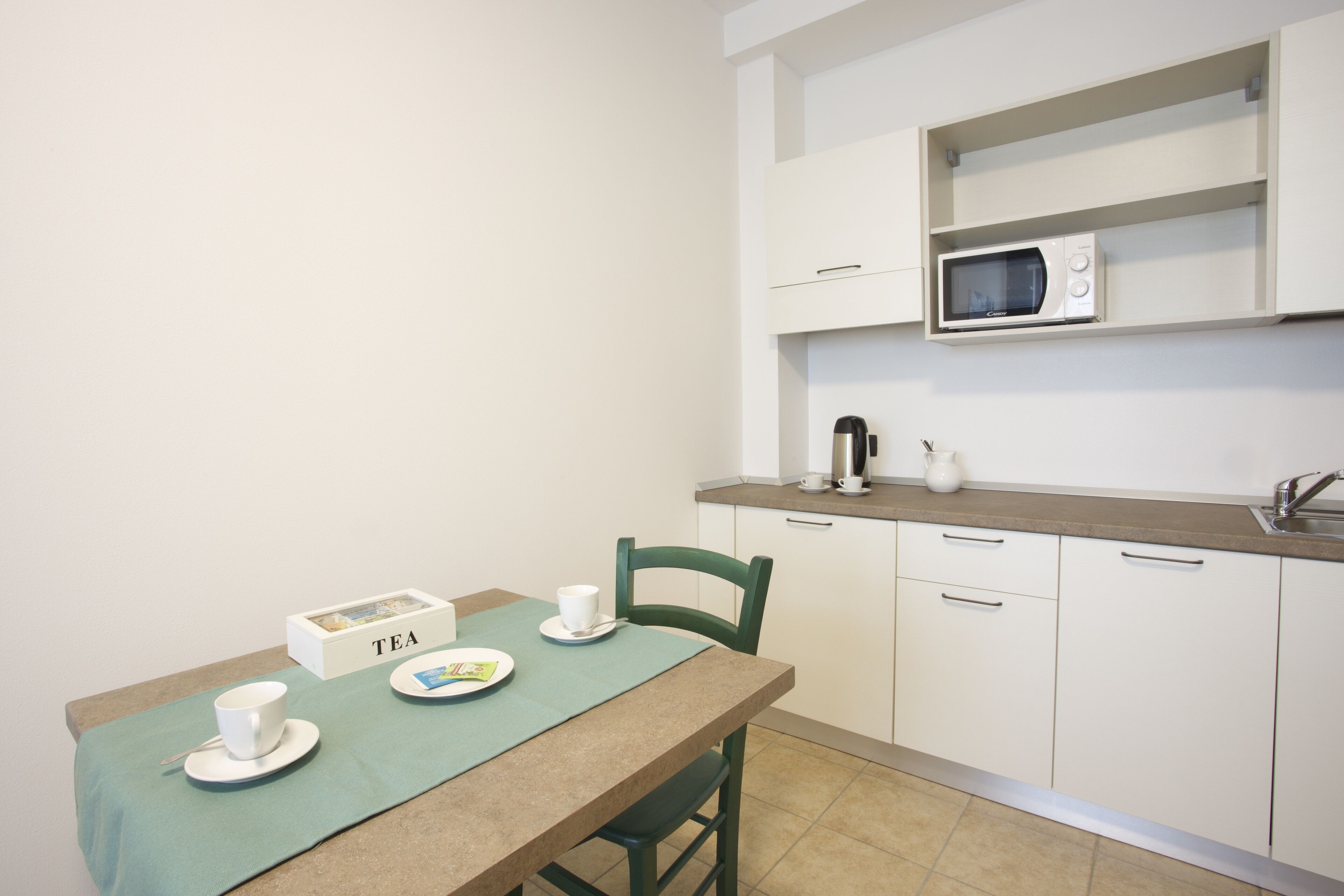 A small kitchenette with a microwave, kettle, and tea set on a table.
