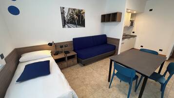 A compact hotel room with a bed, a sofa, a small table, and a kitchenette.