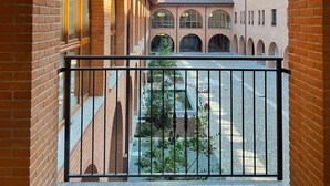 A view through an arched window of a courtyard with a brick building, a metal railing, and a clear sky. - Corte Milano - Hostel (Rozzano)