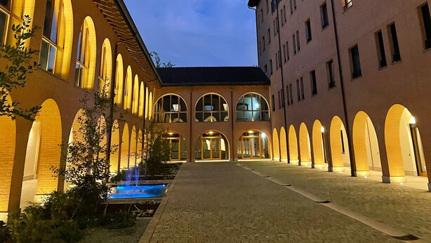 A courtyard with a fountain, arched windows, and a building with multiple floors and balconies. - Corte Milano - Hostel (Rozzano)