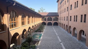 Un patio con edificios de ladrillo, paseos con arcos y una piscina central.