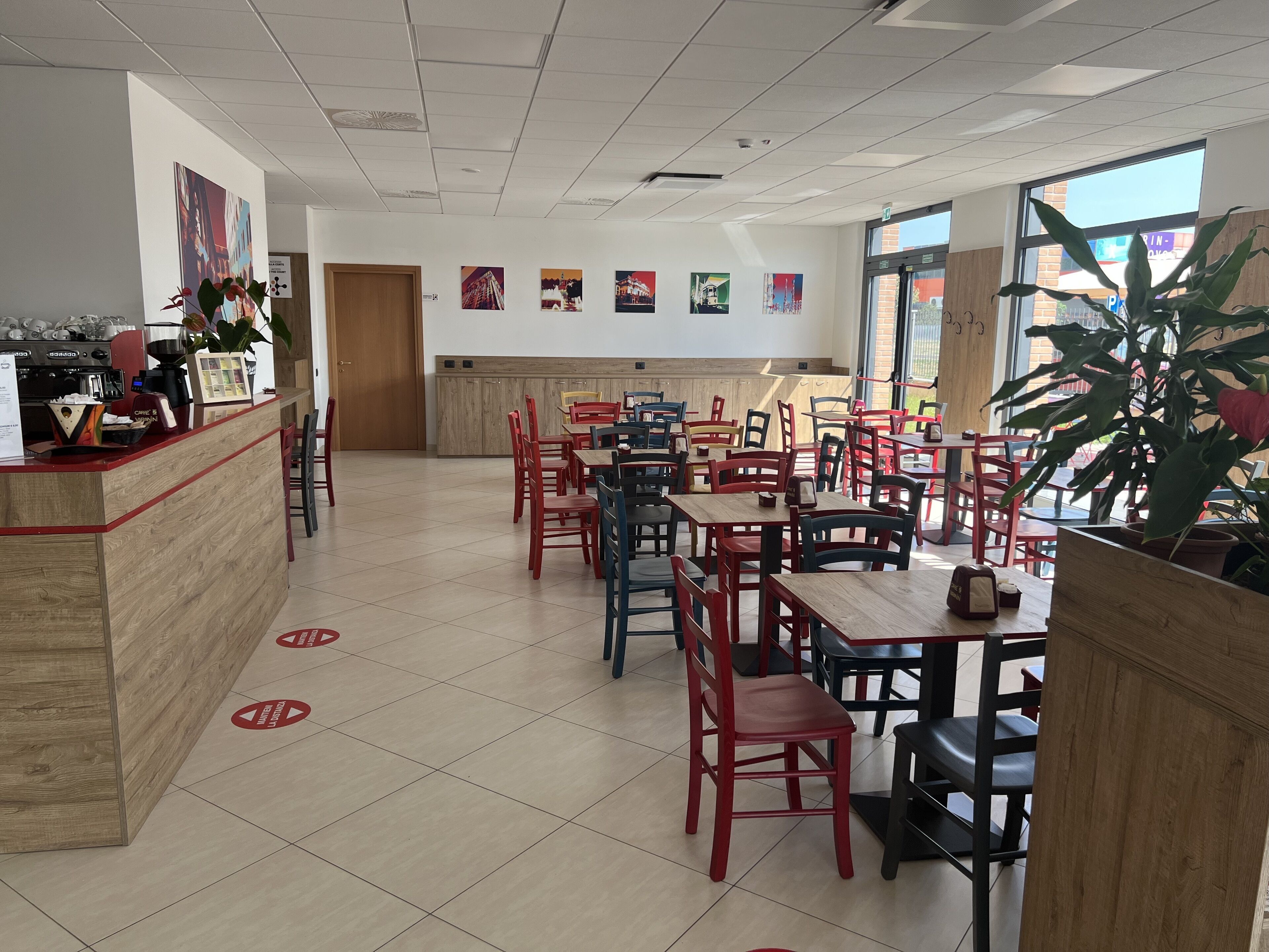 A spacious restaurant with multiple tables and chairs, a counter with a coffee machine, and various wall decorations.