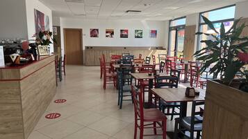A spacious restaurant with multiple tables and chairs, a counter with a coffee machine, and various wall decorations.