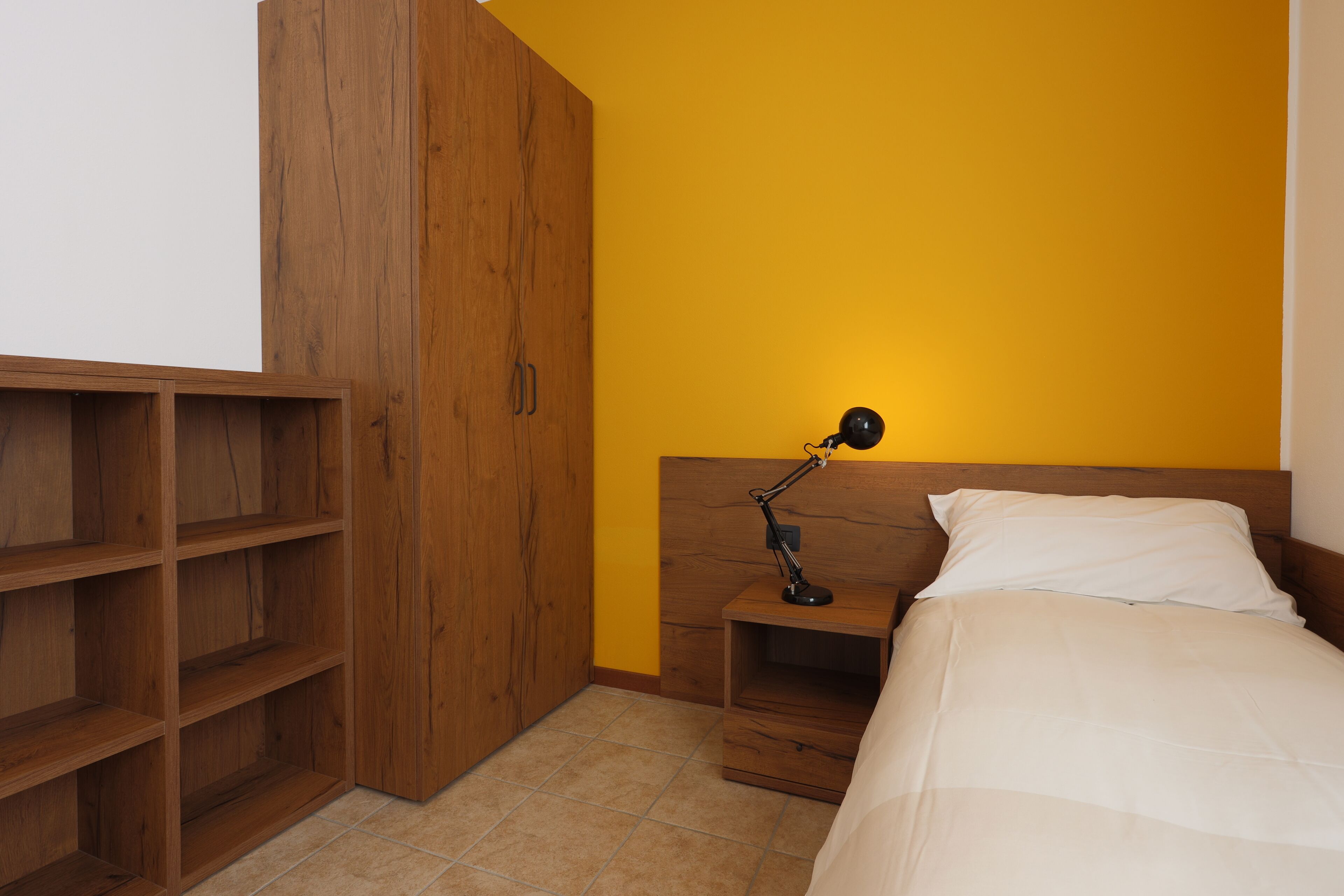 Een slaapkamer met een bed, een nachtkastje, een bureaulamp en een houten garderobe.