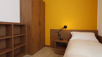Een slaapkamer met een bed, een nachtkastje, een bureaulamp en een houten garderobe.