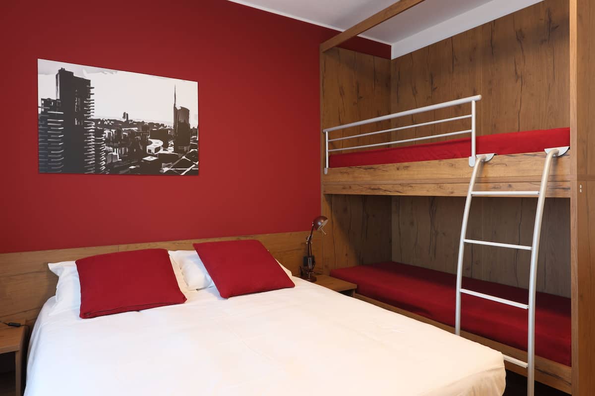 A room with a bunk bed, a wooden headboard, a red wall, and a cityscape painting.