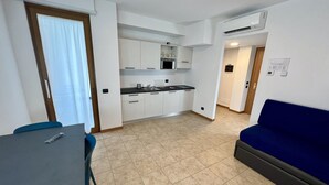 A compact living space with a kitchenette, a dining area, and a sofa. - Corte Milano - Hostel (Rozzano)