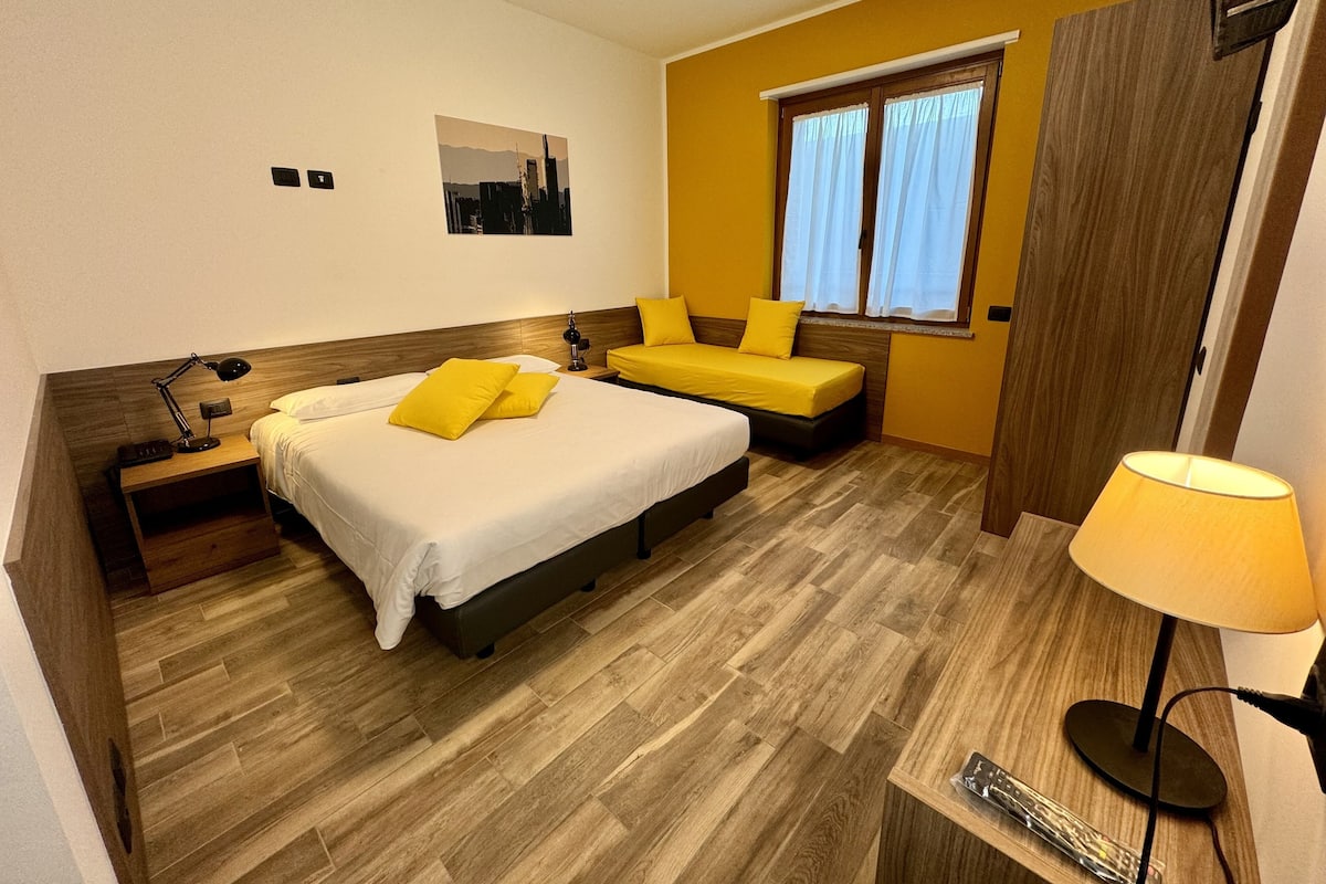 A hotel room with two beds, a desk, a chair, a window with curtains, and a lamp.
