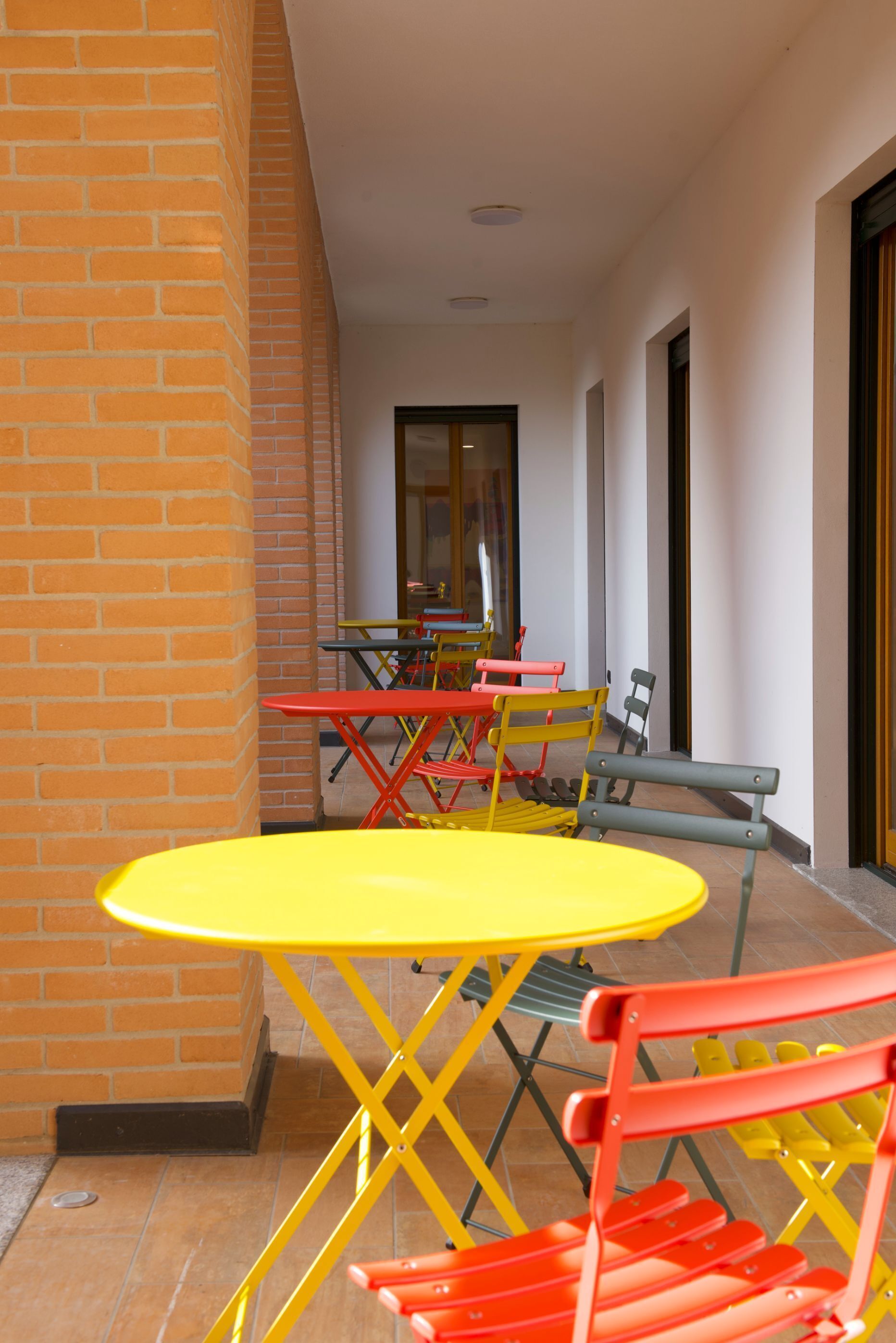 A corridor with a yellow table and red chairs, leading to a room with a door.