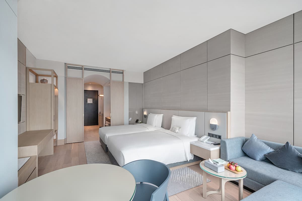 A modern hotel room with a large bed, a sofa, a small table, and a desk.