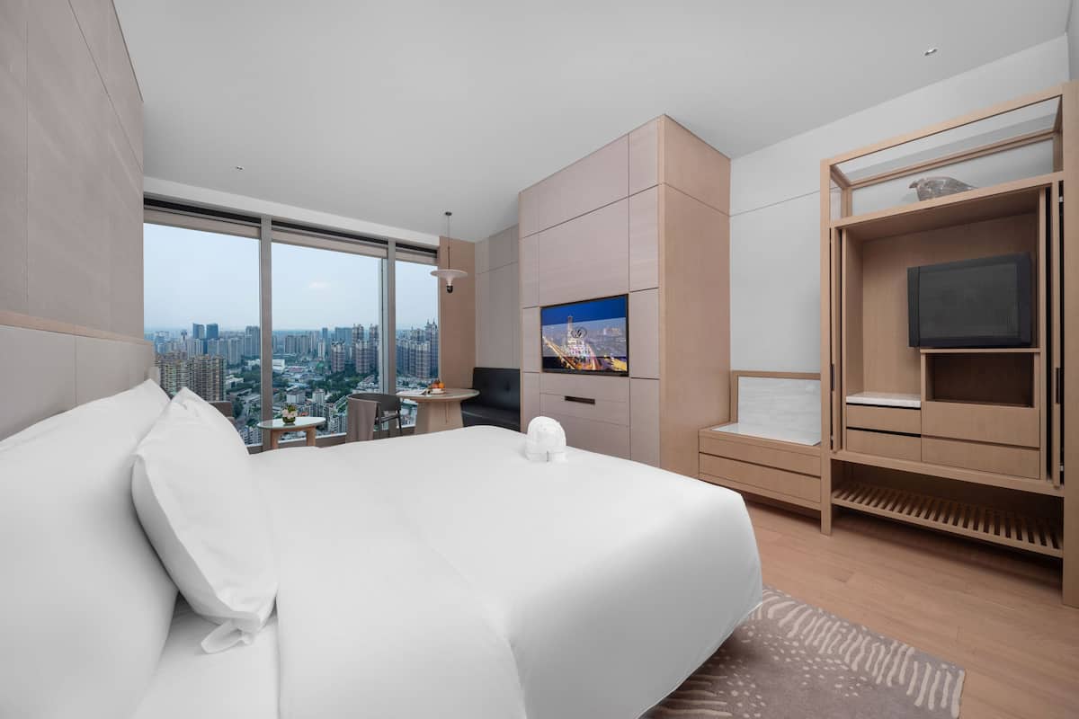 A modern hotel room with a large bed, a TV, a desk, and a city view.