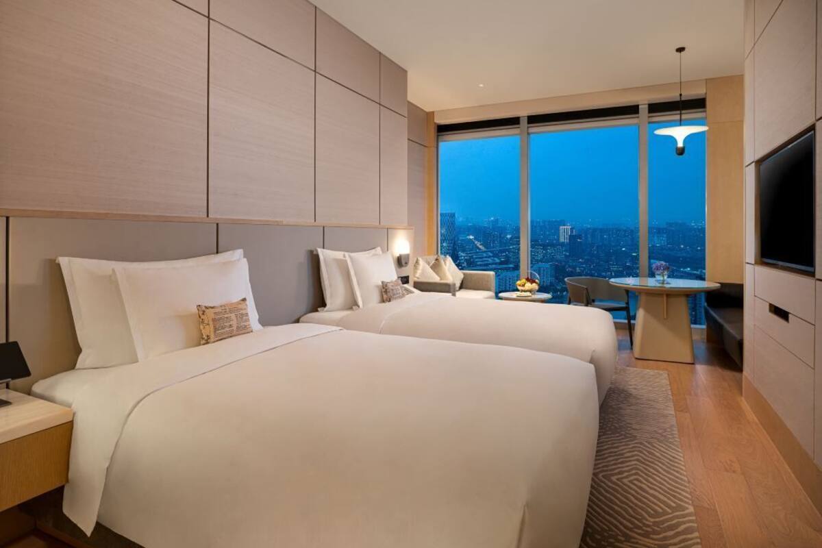 A hotel room with two large beds, a desk, a chair, and a TV.