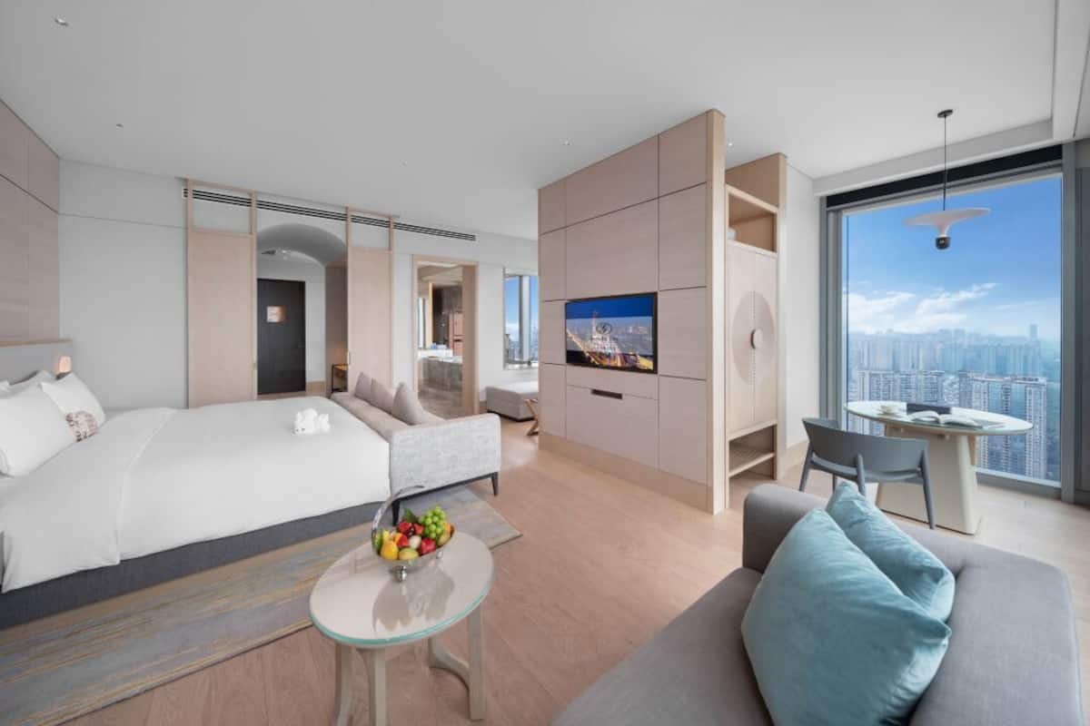 A modern hotel room with a large bed, a sofa, a dining area, and a TV.