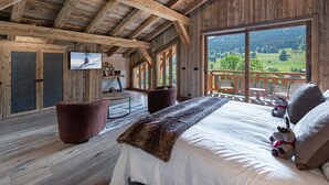 Ein Schlafzimmer einer Holzhütte mit einem großen Bett, einem Fernseher und einem Balkon mit schöner Aussicht.