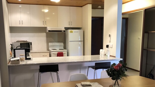 Una cucina moderna con mobili bianchi, un frigorifero bianco e un tavolo da pranzo in legno con quattro sedie.