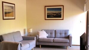 Un soggiorno con soffitto in legno, due divani, una televisione e quadri appesi alle pareti.
