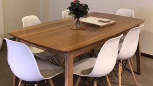Una sala conferenze con un tavolo in legno, sedie bianche, una piccola pianta in vaso e un quadro appeso al muro.