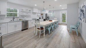 Una cocina moderna con armarios blancos, una isla central con sillas e iluminación colgante.