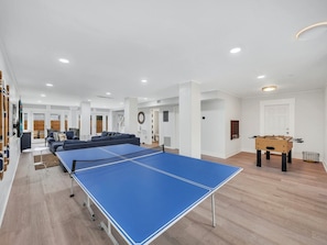 Un grand espace de vie comprenant une table de ping-pong, un ensemble de canapés et une table de baby-foot.