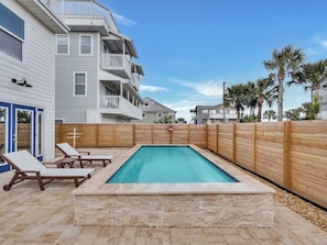 Une piscine avec des chaises longues, une clôture en bois et un bâtiment doté de balcons.