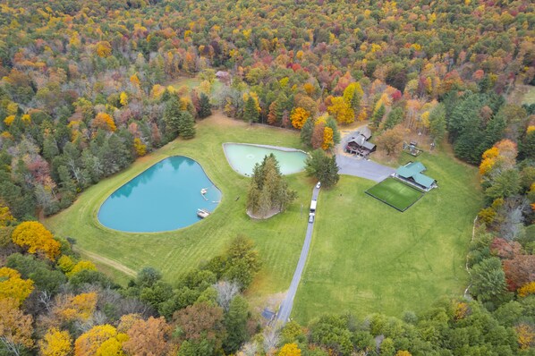 An aerial view of a property with a large pond, a tennis court, and a house surrounded by autumn-colored trees. - A quiet, outback setting, nestled in the mountains of Snyder County (Milroy)