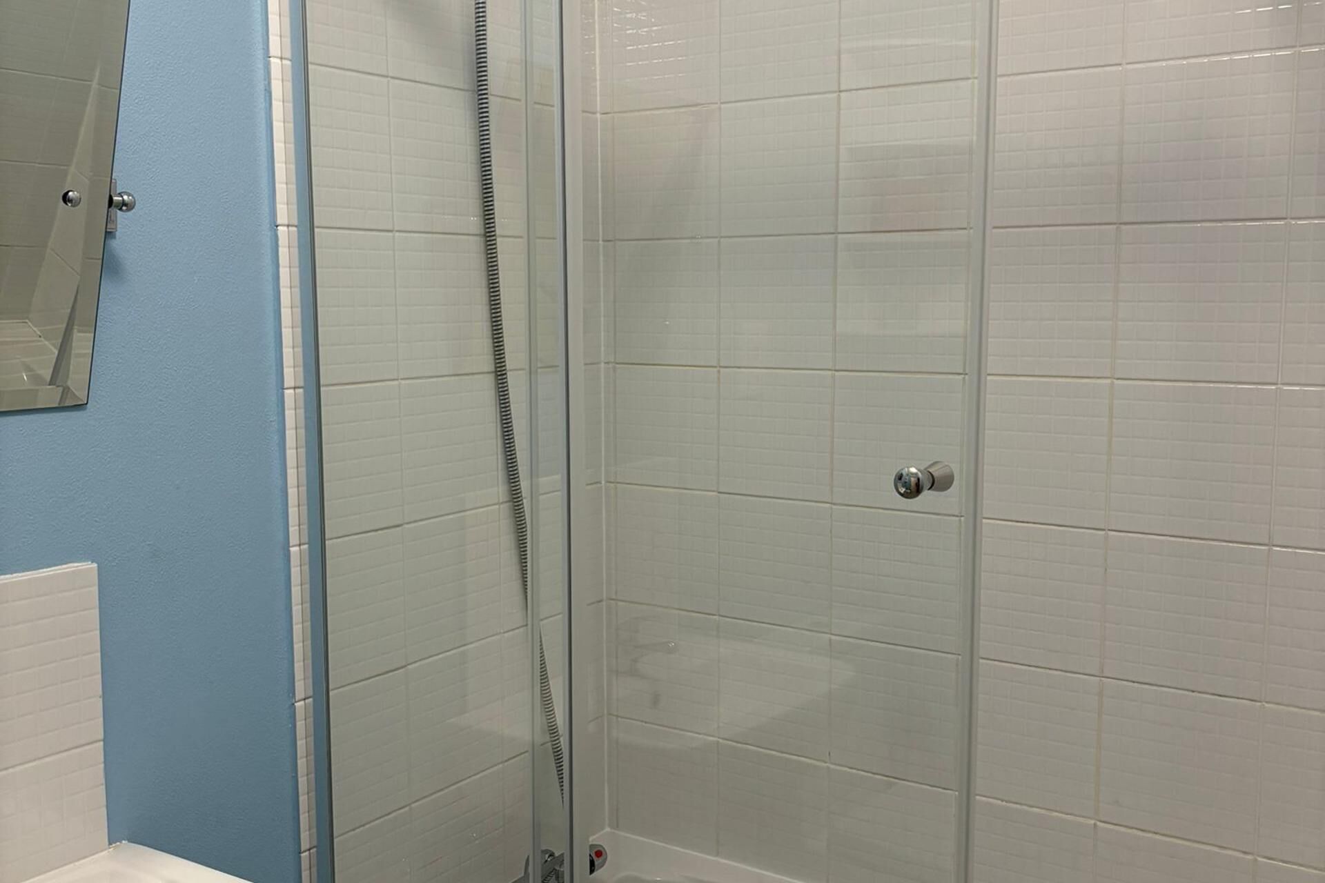 Ducha envuelta en vidrio con azulejos blancos y pared azul.