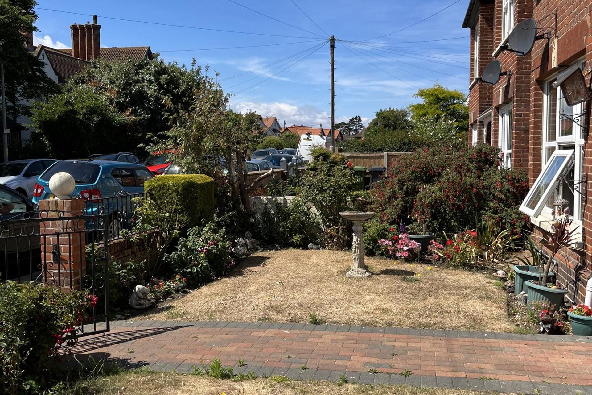 Un jardín residencial con un sendero pavimentado, un bebedero para pájaros y diversas plantas.