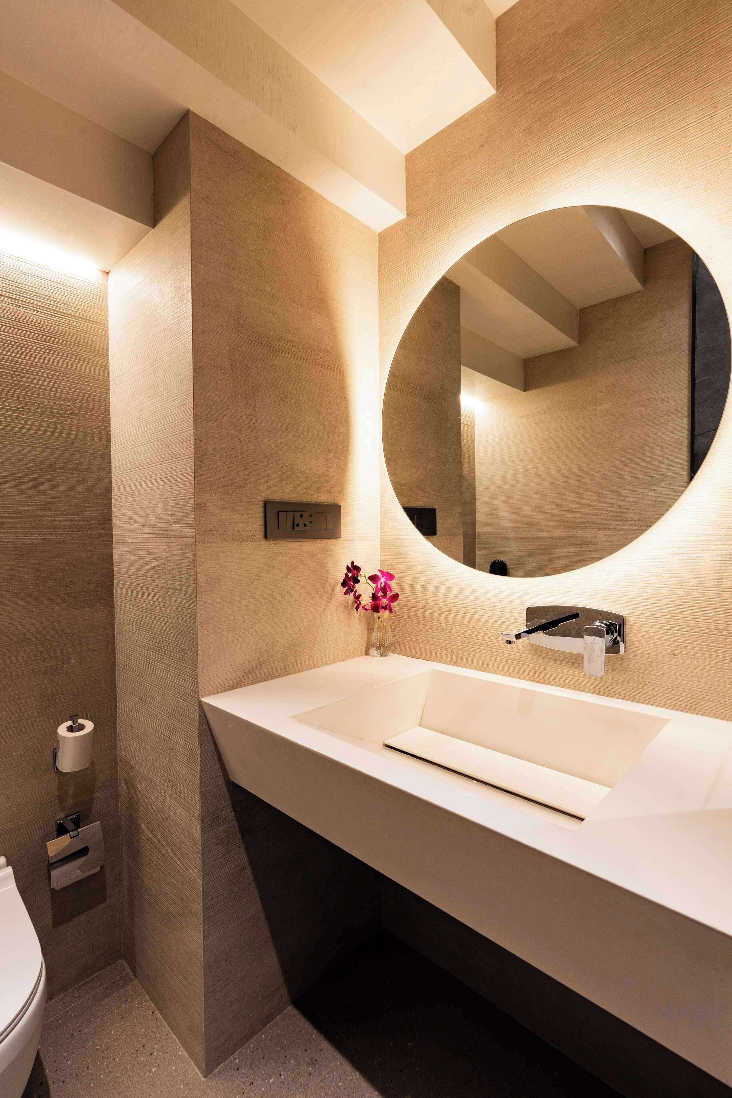 Un baño moderno con un lavamanos grande, un espejo redondo y un florero con flores.