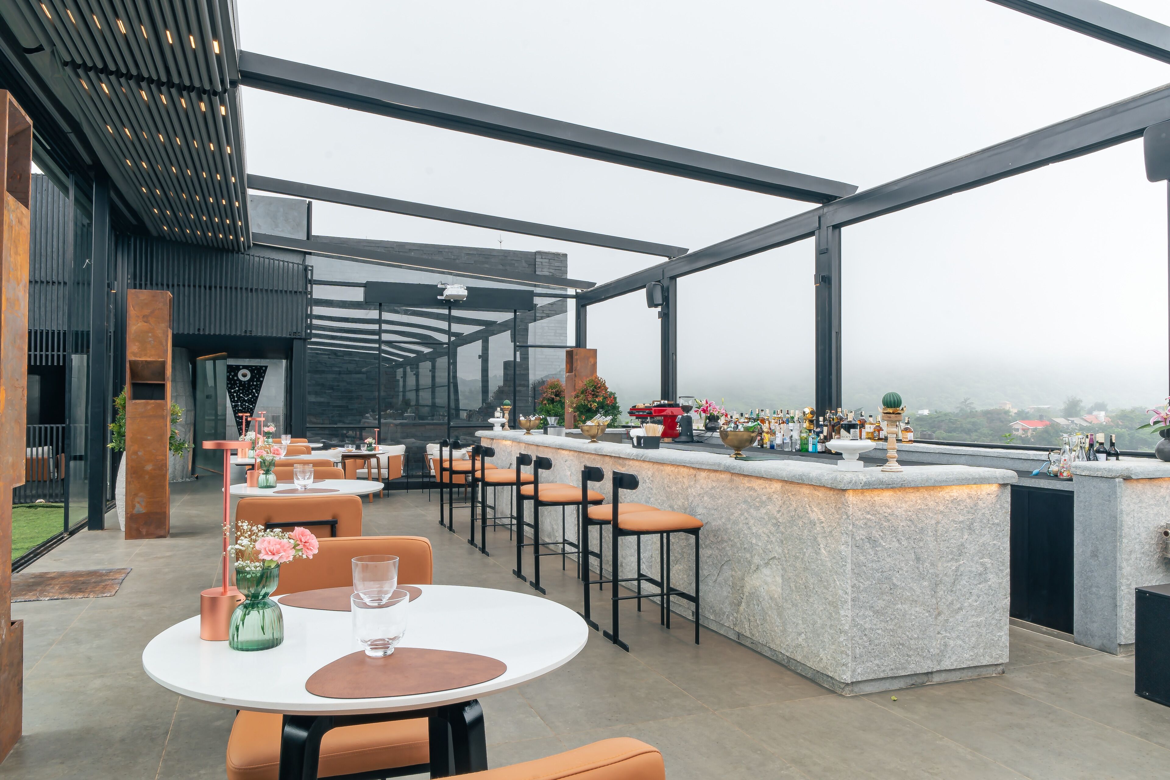 A rooftop bar with a stone counter, bar stools, and tables with chairs.