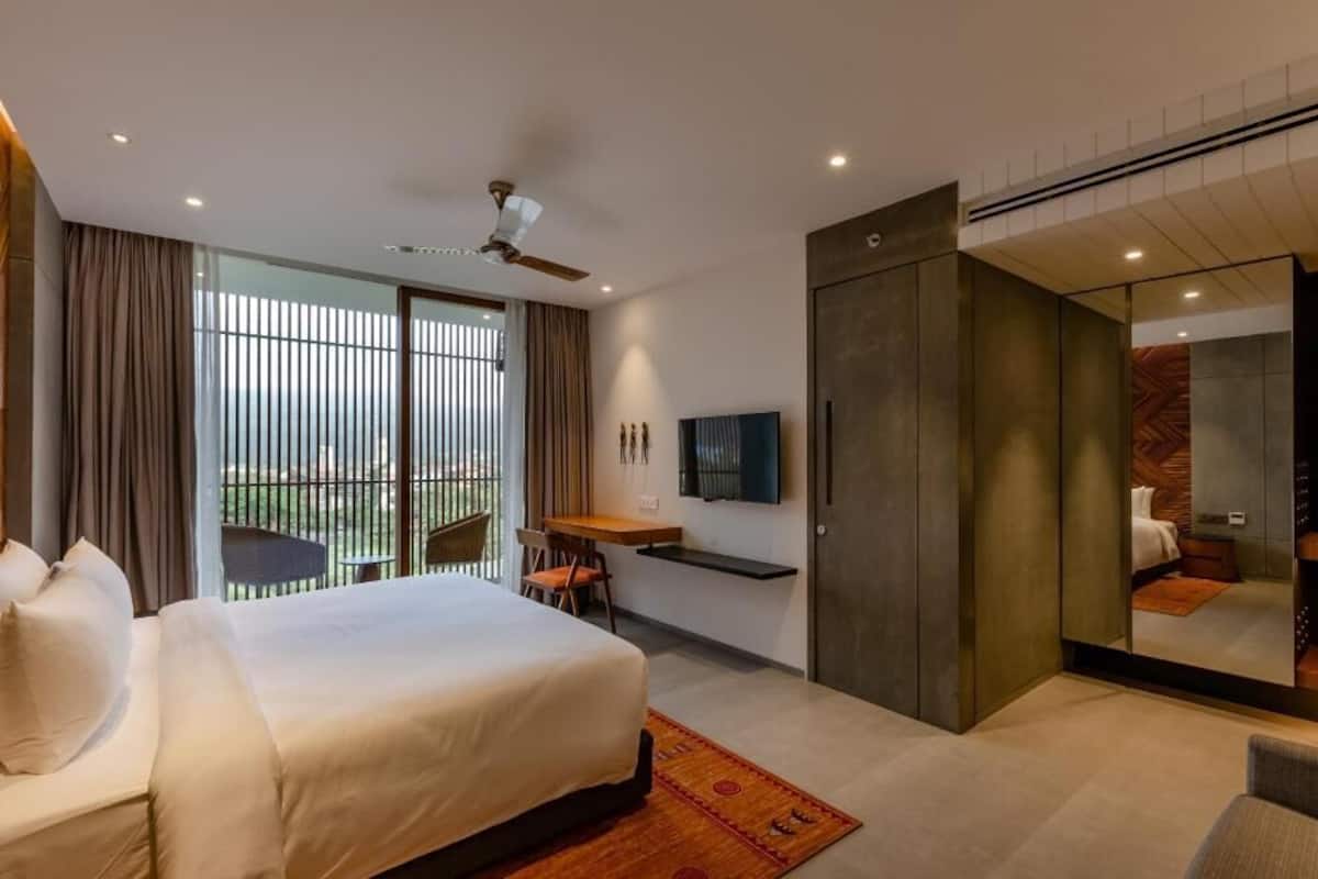 A hotel room with a bed, a desk, a chair, a TV, and a sliding door leading to a balcony.