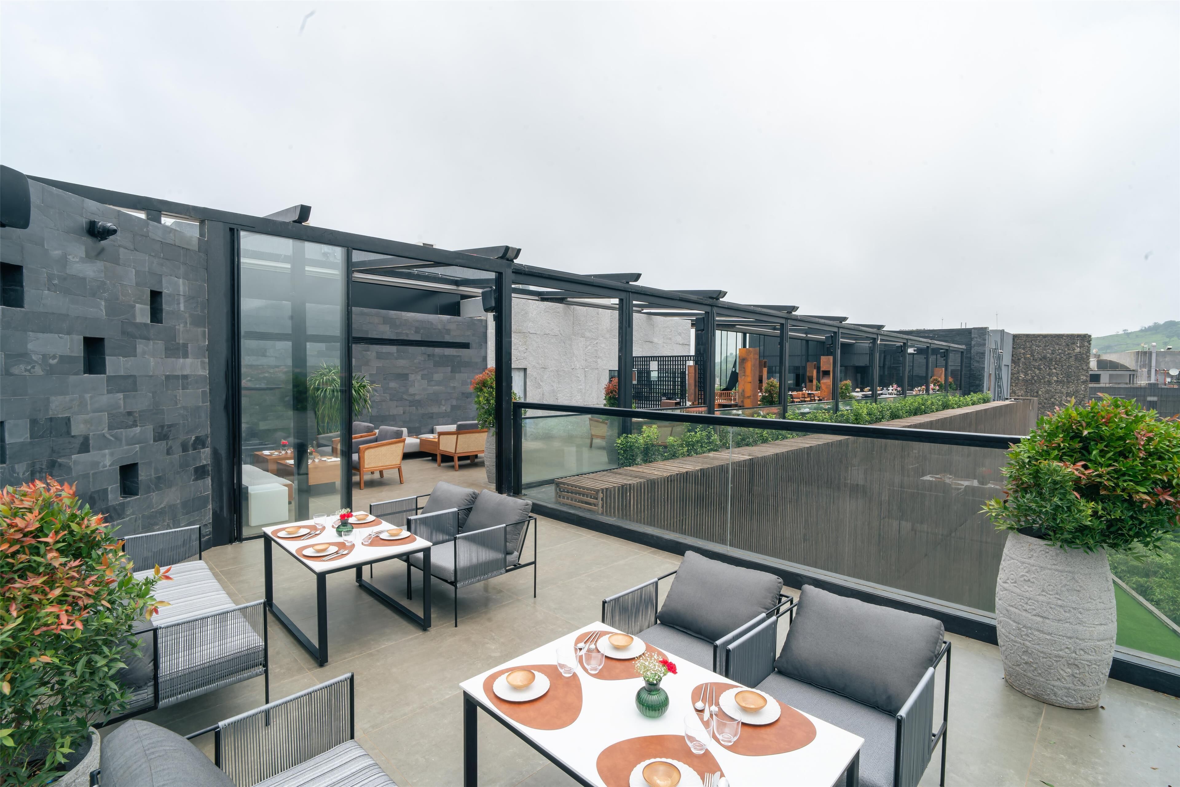 A modern outdoor dining area with glass walls, contemporary furniture, and a view of the cityscape.
