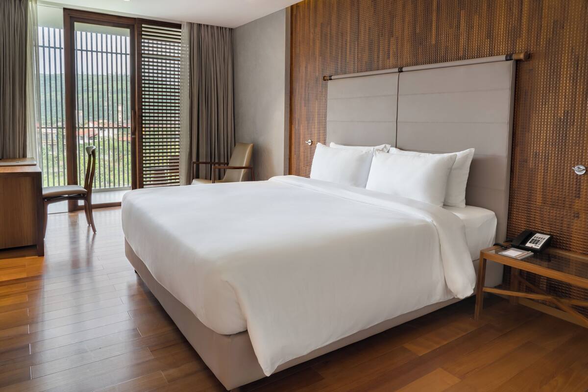 A hotel room with a large bed, a wooden floor, a desk with a telephone, and a chair.