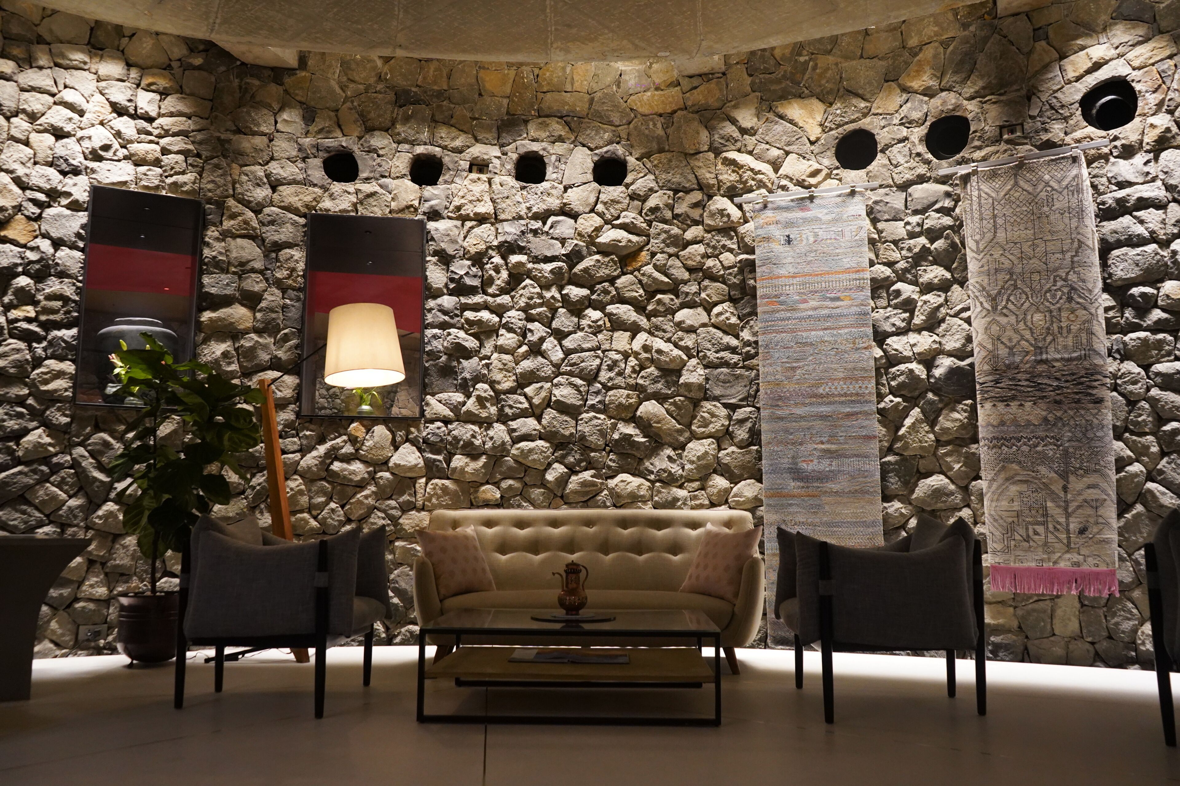 A stone wall interior with a sofa, two chairs, a table, and a lamp.