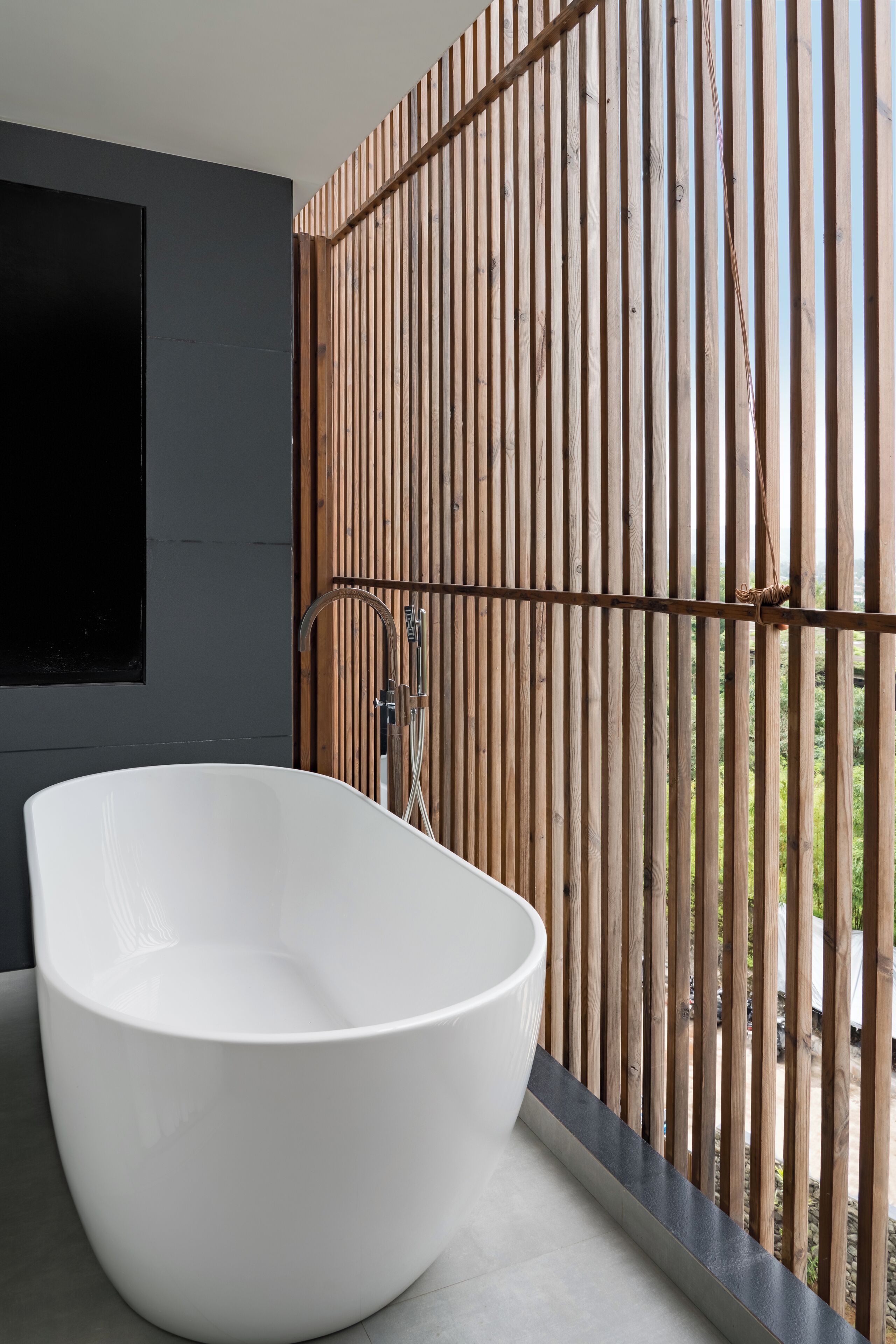 Un baño moderno con una bañera independiente, un separador de madera con listones y vistas exteriores.