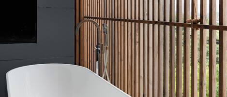 Un baño moderno con una bañera independiente, un separador de madera con listones y vistas exteriores.