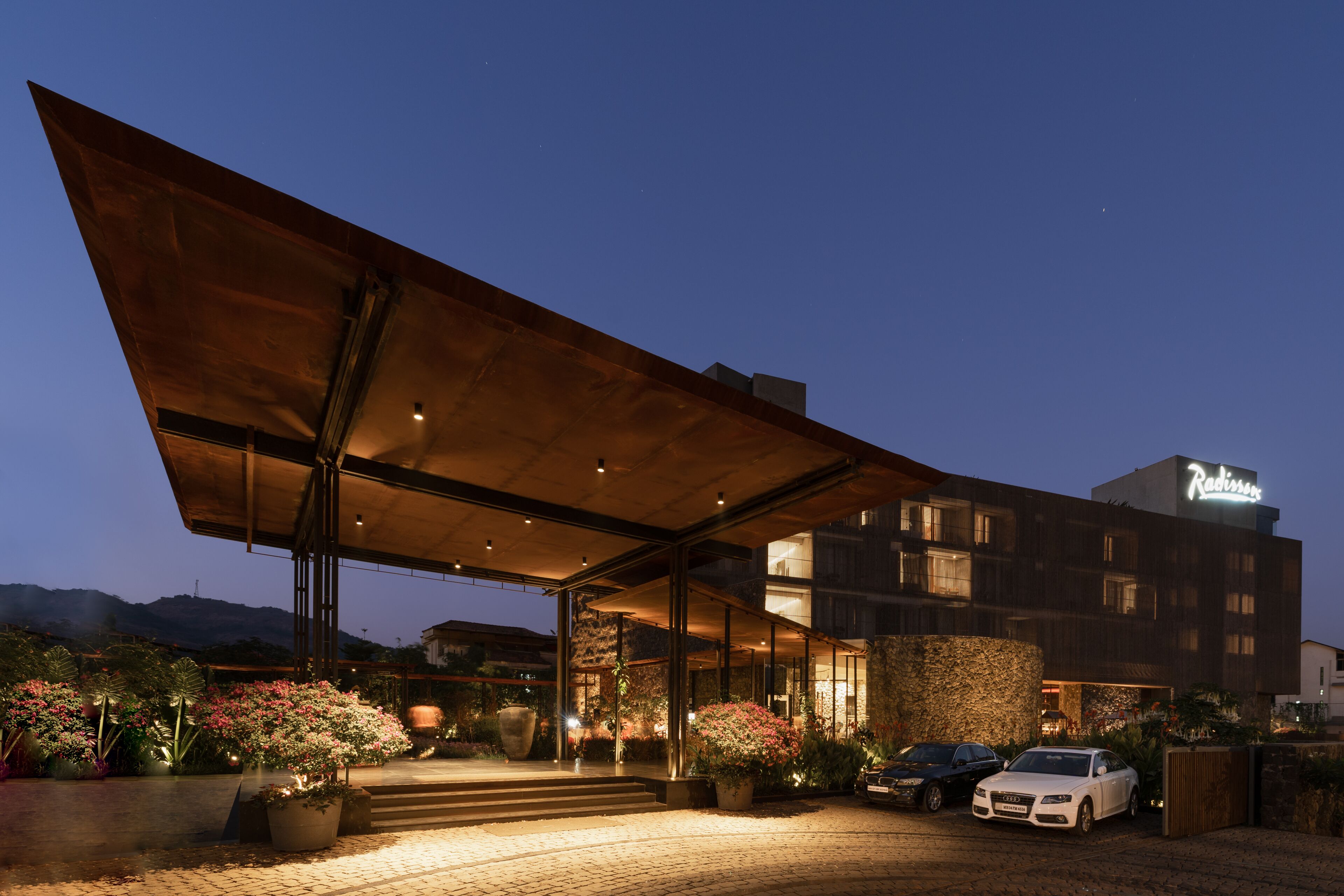 Un hotel moderno con vestíbulo cubierto, fachada de piedra y un automóvil estacionado frente a él.