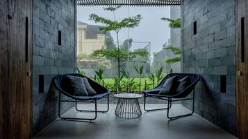 A modern interior with two wicker chairs and a small round table, set against a backdrop of a brick wall and a view of greenery outside.