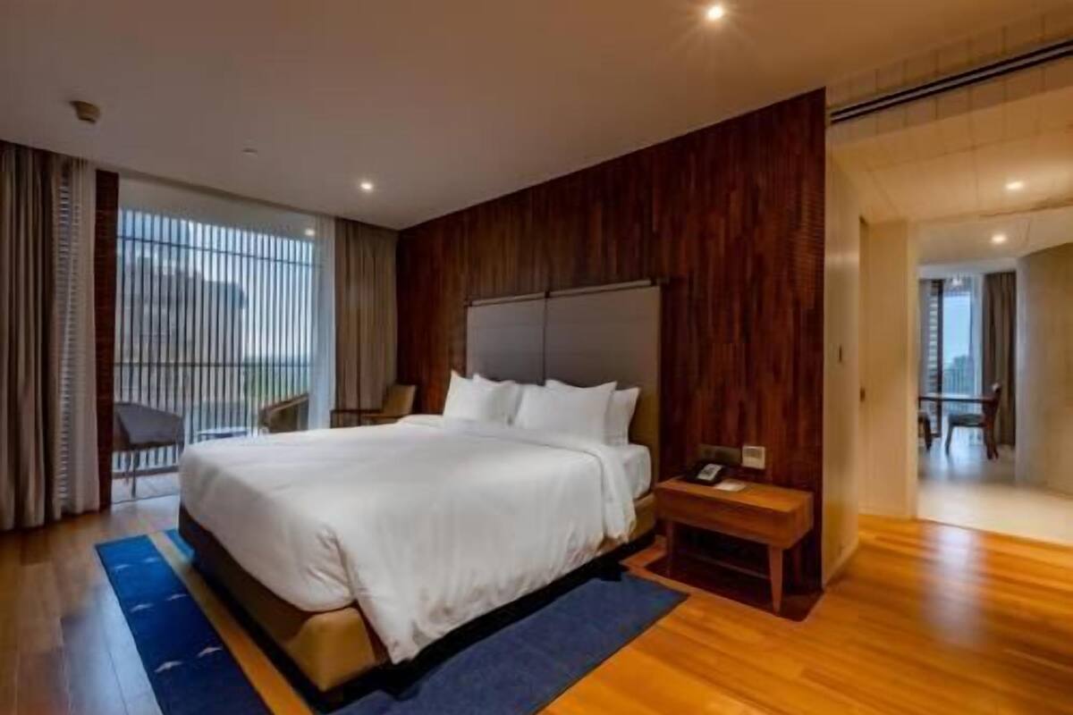 A hotel room with a large bed, a wooden headboard, a nightstand, and a view of the outside.
