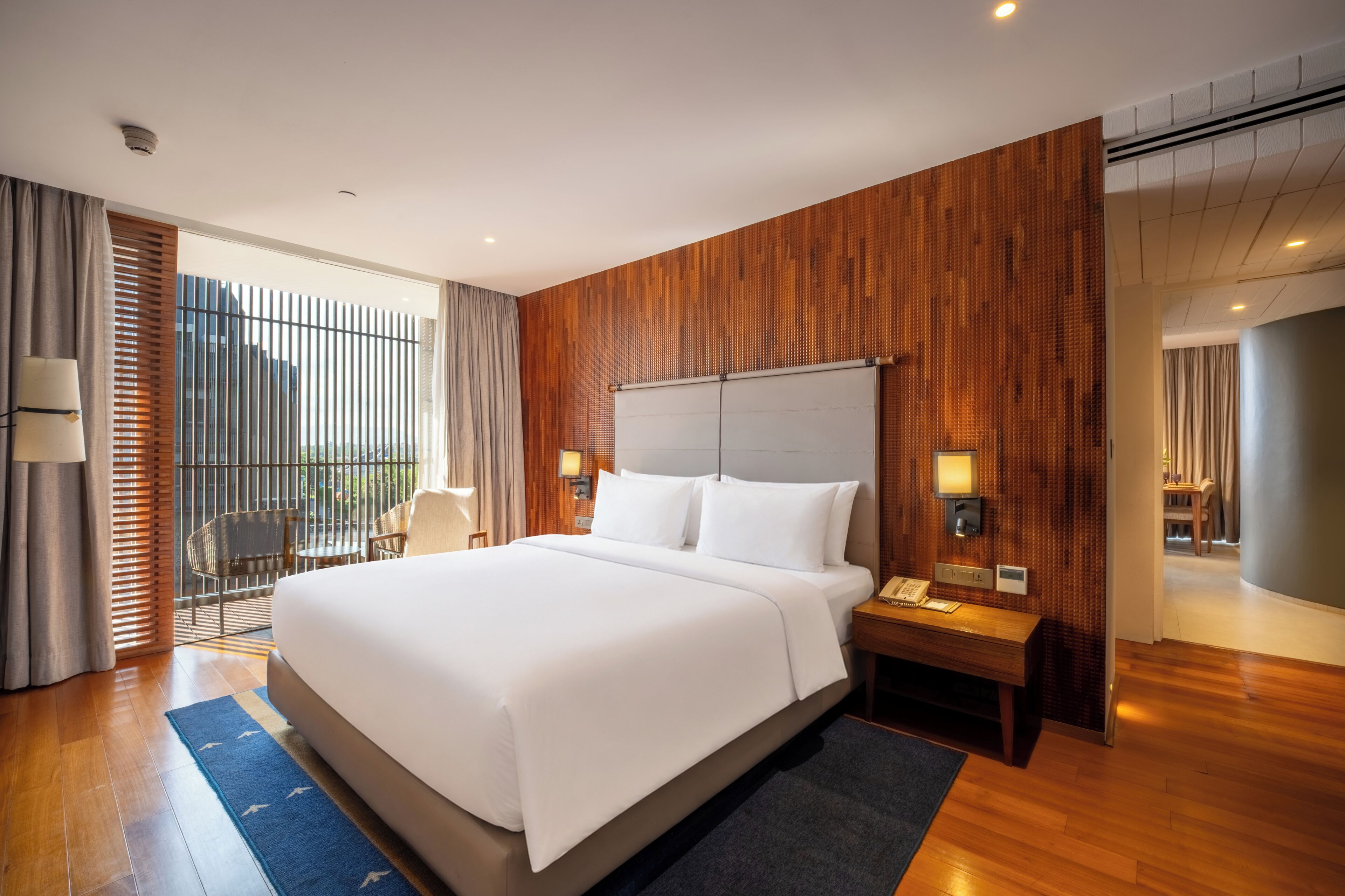 A hotel room with a large bed, a desk with a lamp, a chair, and a view of the outdoors.